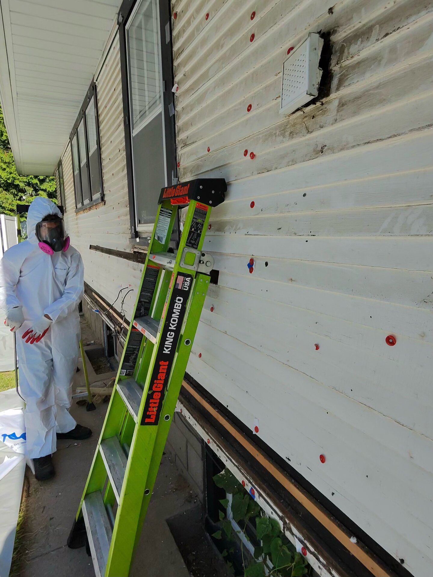 Top Priority technician in full hazmat suit and respirator performing asbestos abatement on an Oklahoma exterior